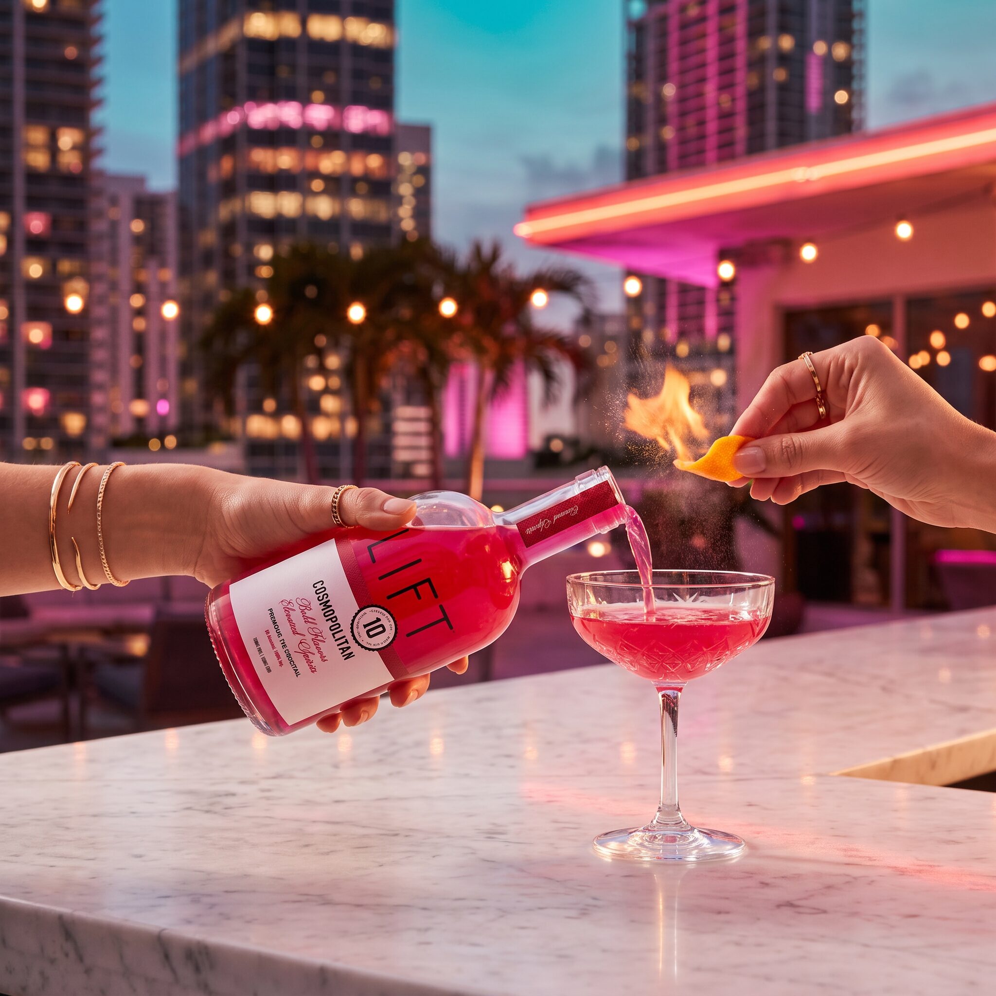 Two hands pouring the LIFT Cosmopolitan into a coupe on a Miami rooftop bar at dusk, flamed orange peel over the surface, Brickell skyline behind
